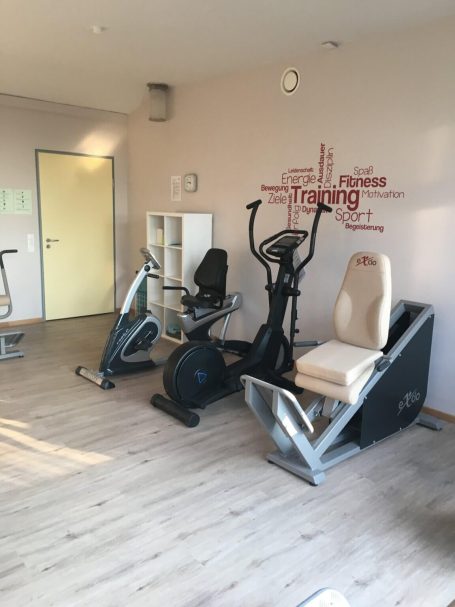 Fitnessraum mit zwei Trainingsgeräten: einem Crosstrainer und einem Drehsitz.